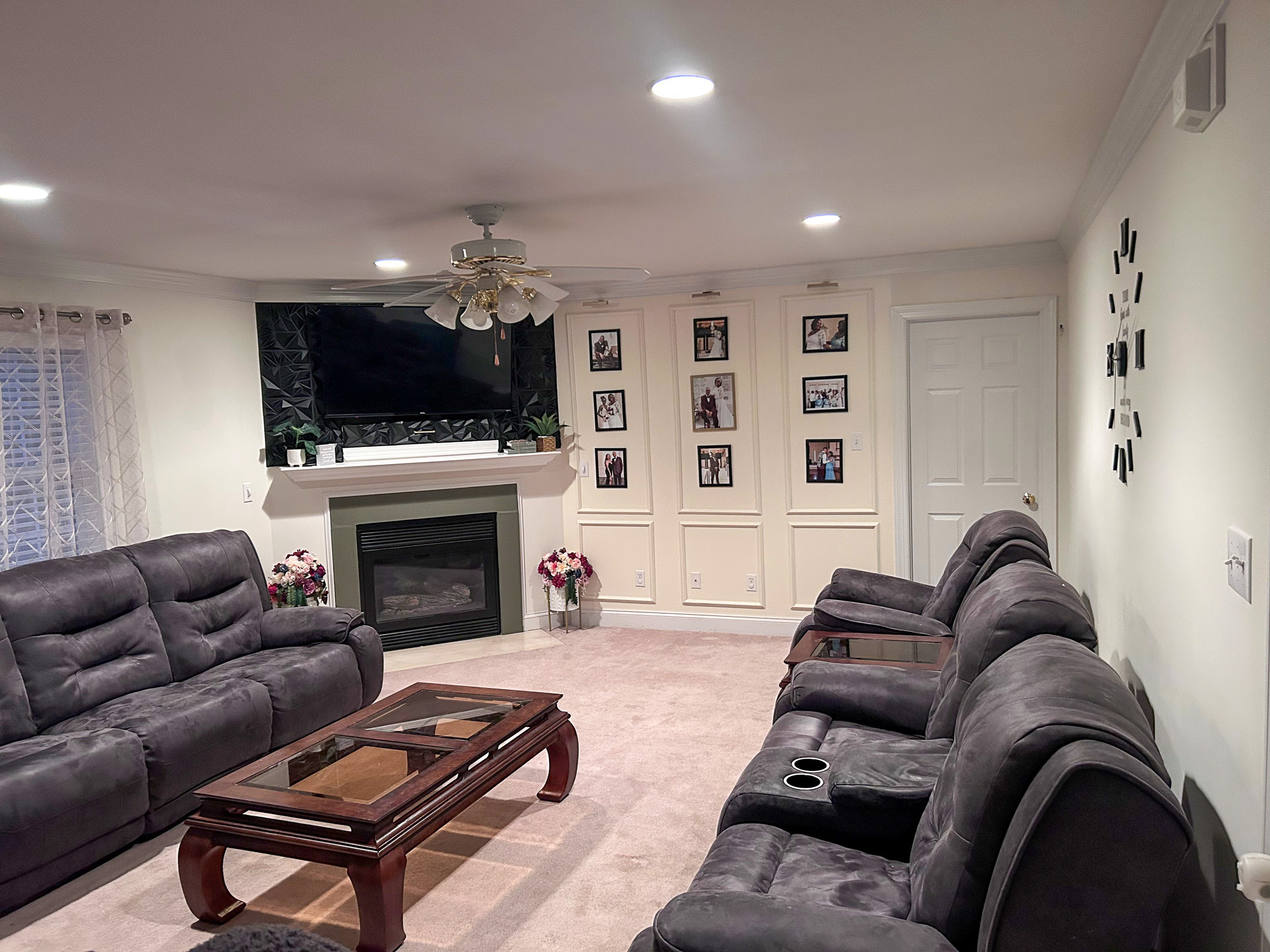 Cozy living room with reclining sofas, a wall-mounted TV above a fireplace, family photos on the wall, and soft lighting belonging to Sponsored Residential Provider Wanette and Carol Spencer in Richmond, Virginia.