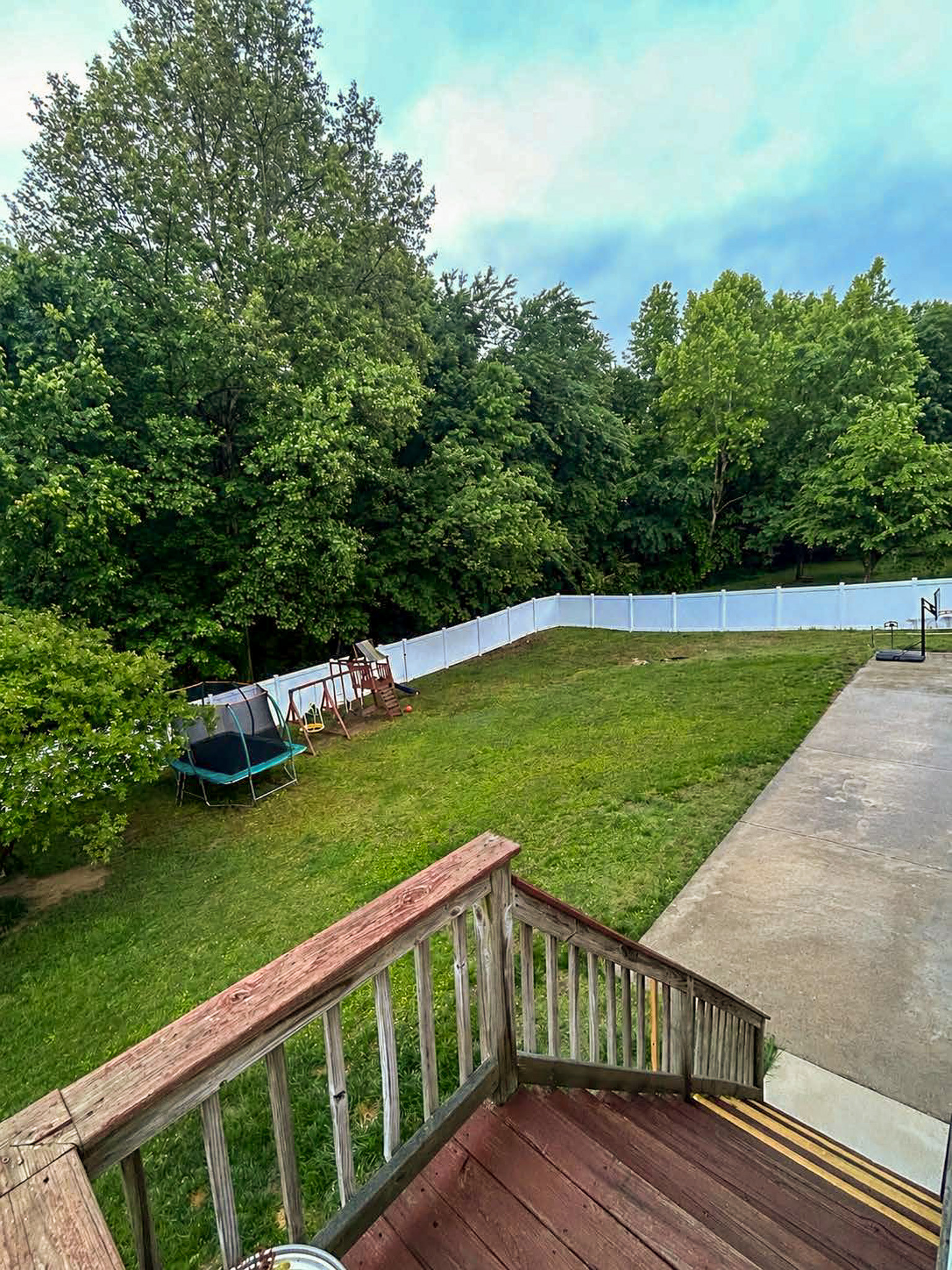 Large fenced backyard with green lawn, playset, trampoline, patio area, and wooden deck steps, surrounded by trees belonging to Sponsored Residential Provider Wanette and Carol Spencer in Richmond, Virginia.