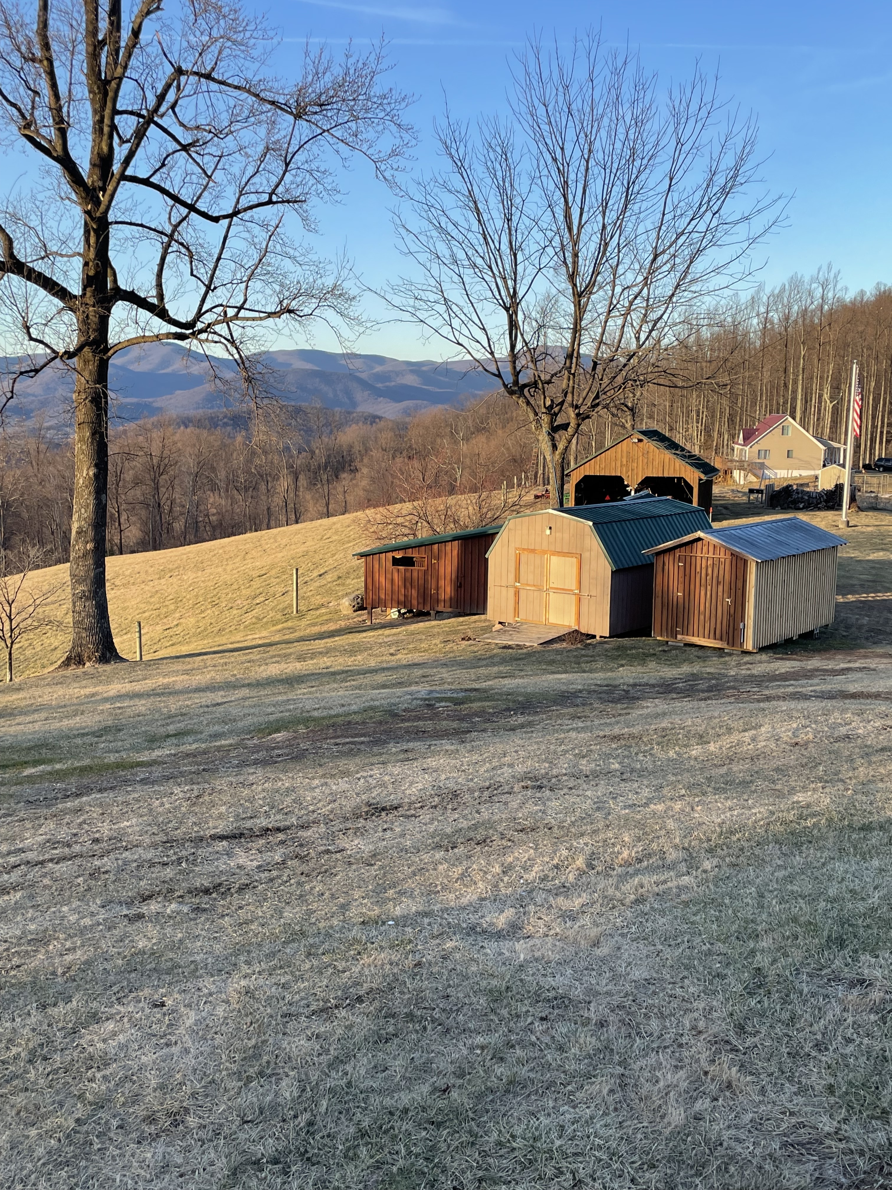 Frost‑covered grassy yard with several small wooden sheds, bare trees, and rolling hills with mountains in the distance under a clear sky at the home of Sponsored Residential Providers Jimmy and Nancy Ayers in Monroe, Virginia.