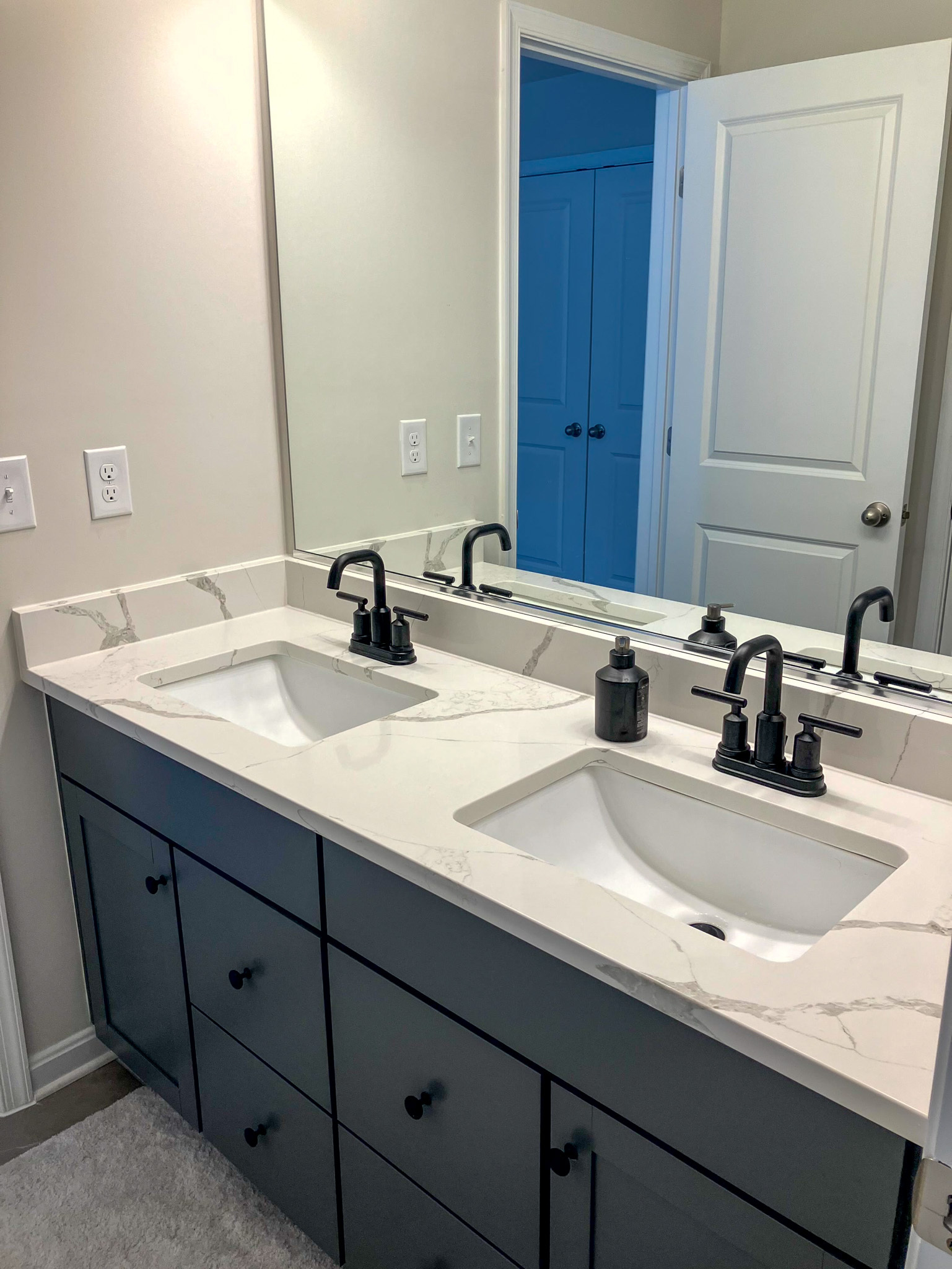 Bathroom vanity with two white sinks, black faucets, and a large mirror above dark cabinets  inside the home of Sponsored Residential Provider Homaira Yazdani in Fredericksburg, Virginia.