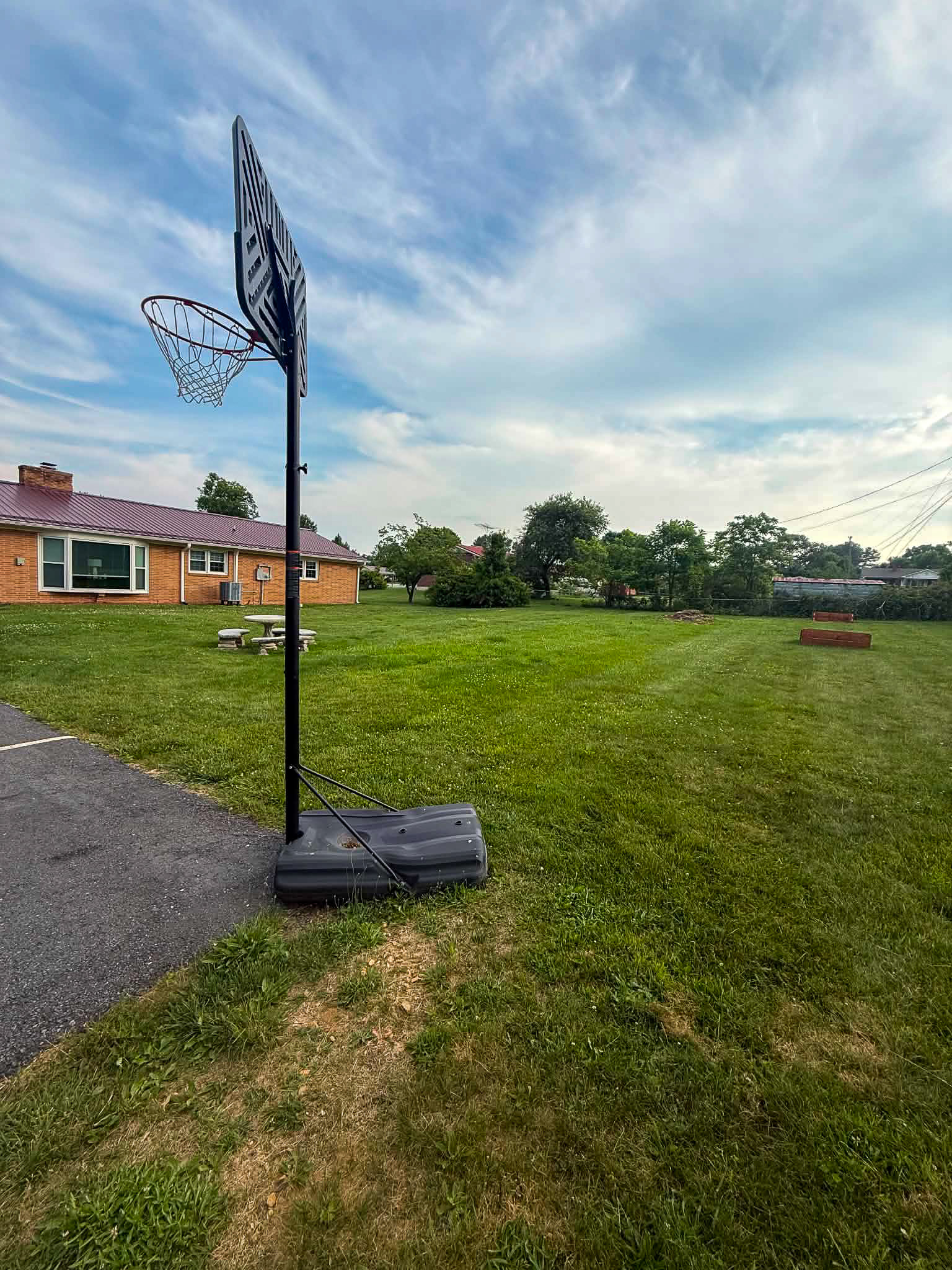 Provider group home in Galax, Virginia belonging to Dylan Mays featuring a portable basketball hoop on paved drive beside a large grassy yard with brick building and trees under a cloudy sky.