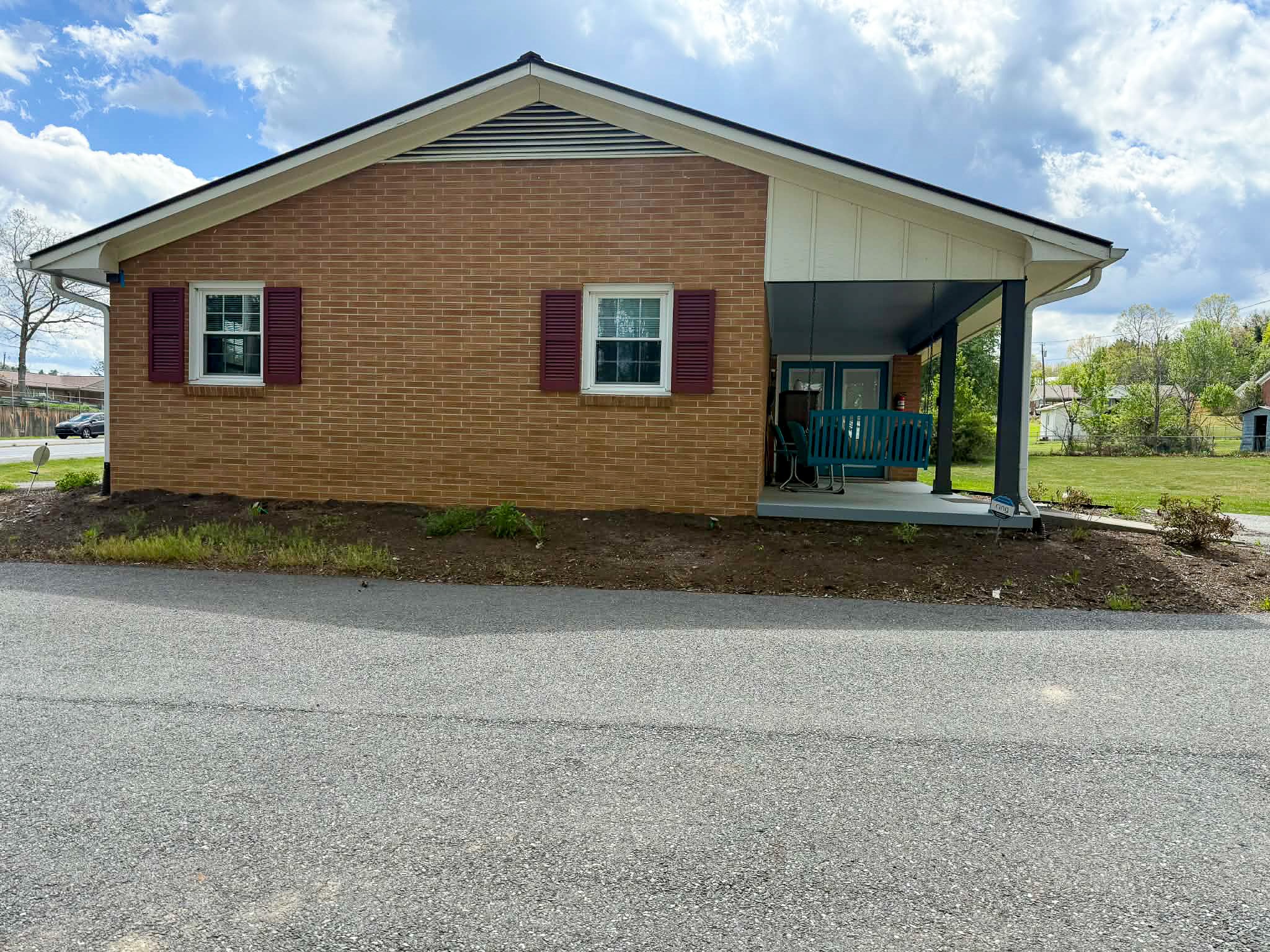 Side view of single-story brick house with red shutters and small covered porch with teal railing outside the home of Group Home Provider Dylan in Galax, Virginia