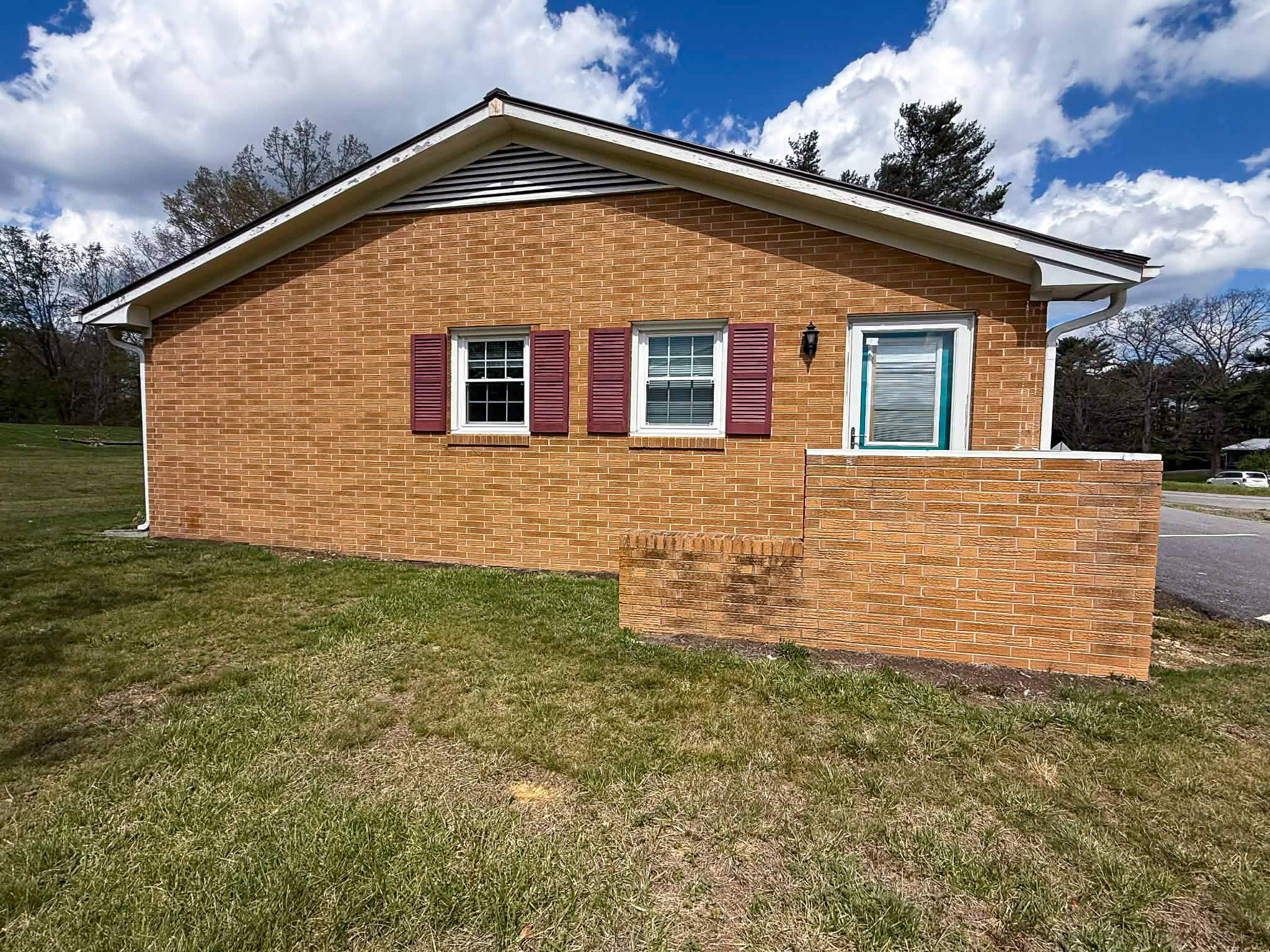 Side view of brick house with red shutters, small enclosed porch entry, and grassy yard outside the home of Group Home Provider Dylan in Galax, Virginia