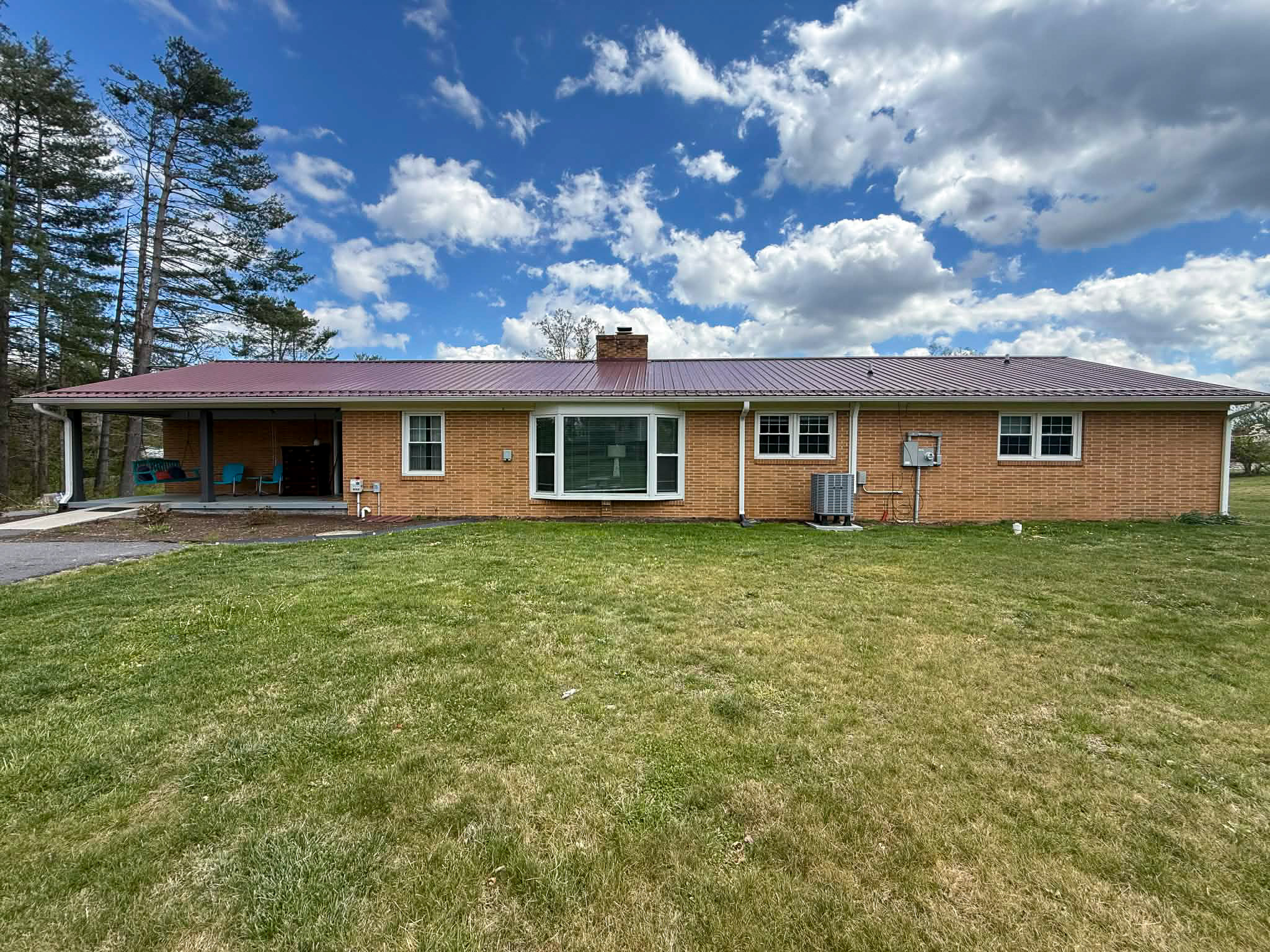 Rear view of single-story brick home with red metal roof, covered patio seating, and open backyard lawn belonging to Group Home Provider Dylan in Galax, Virginia
