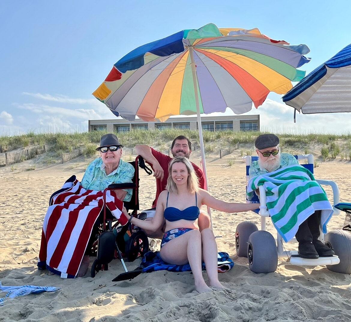 Two providers with twin individuals at the beach on a sunny day posing under an umbrella in the sand.