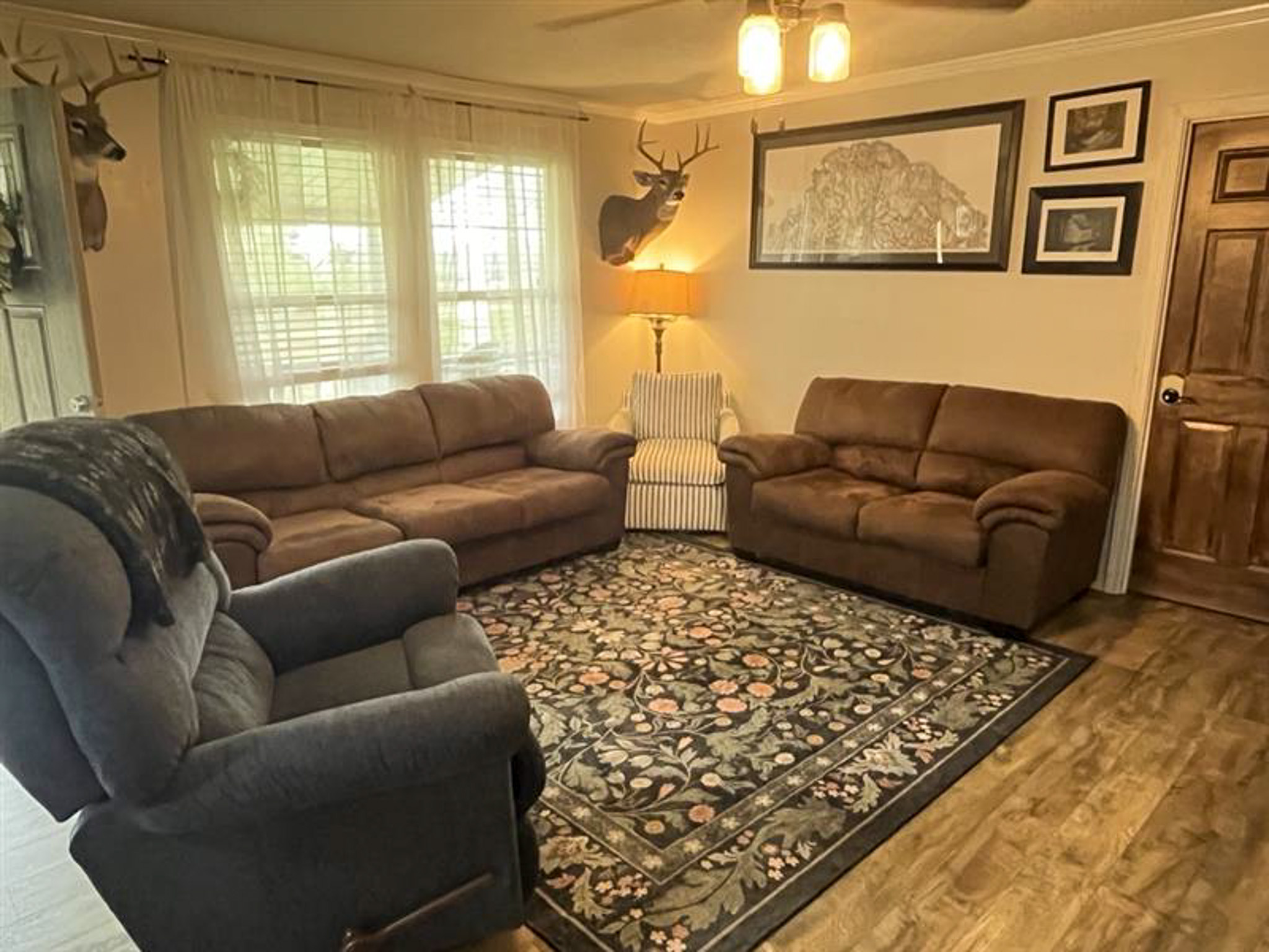 Living room with sofas, armchair, patterned rug, wall art, and mounted deer décor inside the home of Sponsored Residential Provider Kristen Bowers in Galax, Virginia.