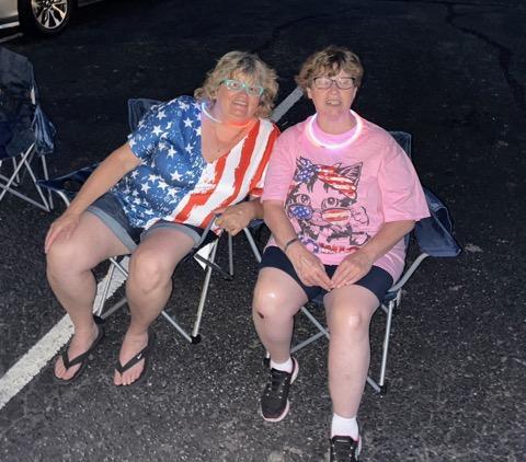Two women sitting in lawn chairs outdoors celebrating the fourth of July at night time.
