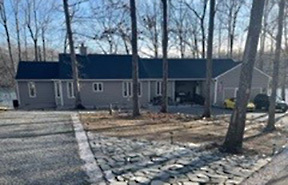 Single‑story home with tan siding, dark roof, gravel driveway, and leafless trees in a wooded setting belonging to Group Home Provider Ana Garcia in Spotsylvania, Virginia.