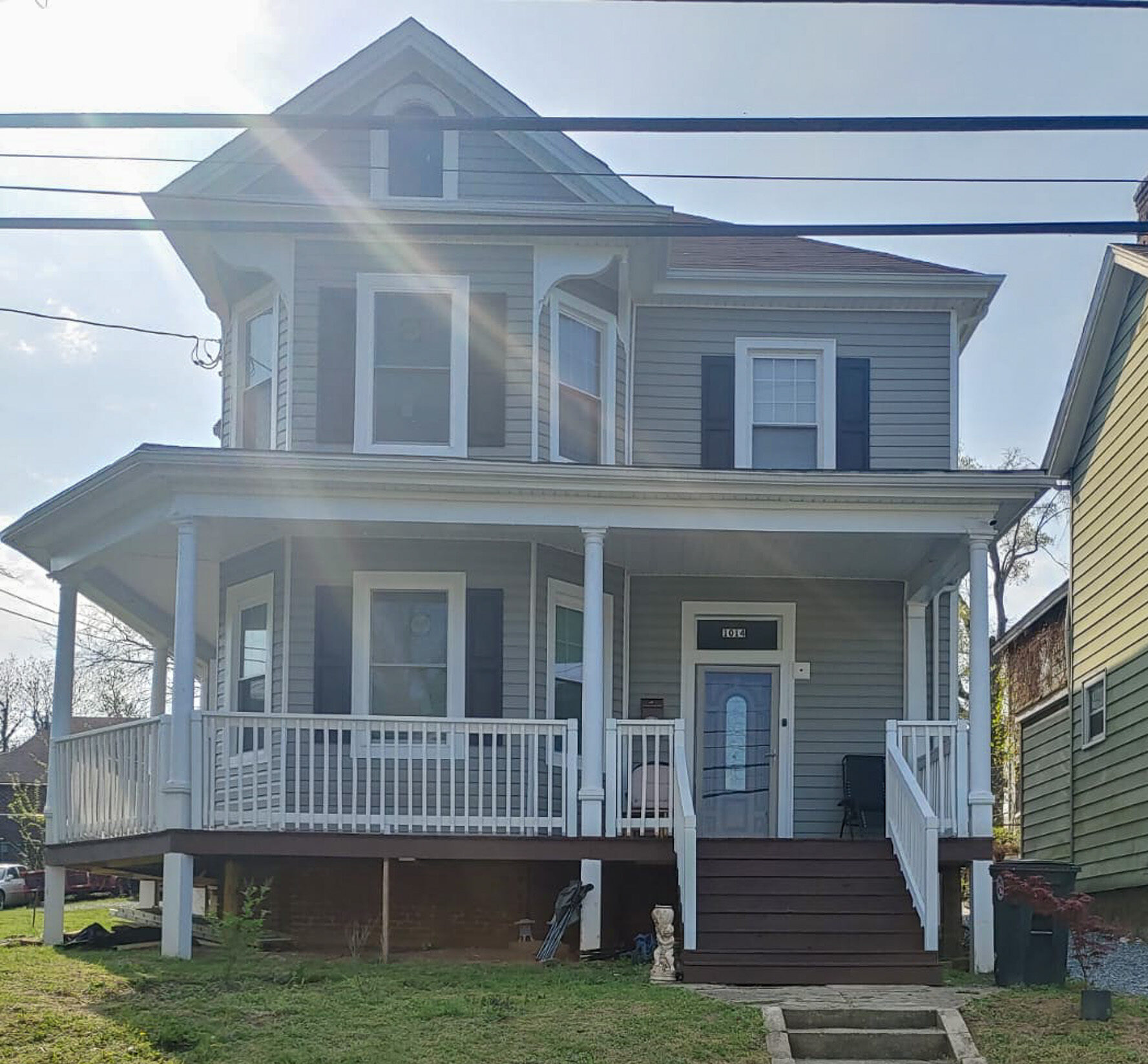 Two‑story gray house with a large wraparound porch, dark shutters, and steps leading up from the front yard belonging to Sponsored Residential Providers Gladys and Victor Oluwaji in Lynchburg, Virginia.