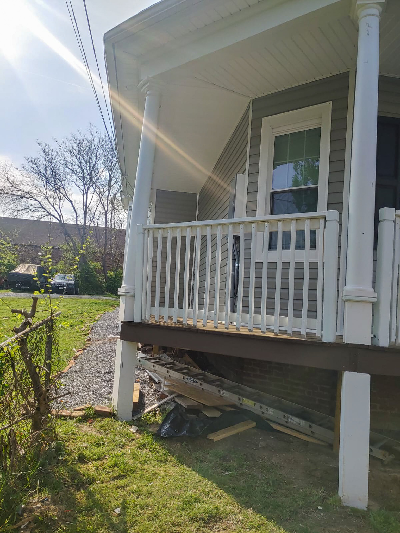 Side view of a house’s front porch with white railings and columns, sunlight streaming across the scene, and a grassy yard beside a stone walkway belonging to Sponsored Residential Providers Gladys and Victor Oluwaji in Lynchburg, Virginia.