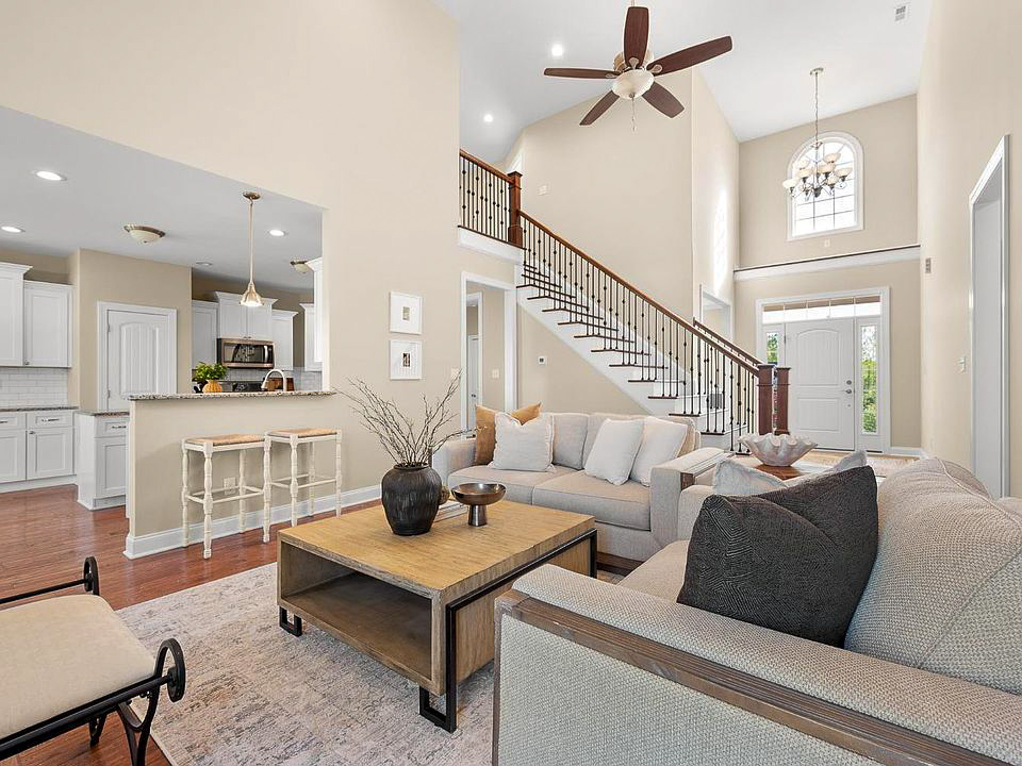 Bright living room with high ceilings, neutral décor, and a staircase overlooking the space, connected to an open kitchen area in the home of sponsored residential provider Lisa Reed in Lynchburg, Virginia.