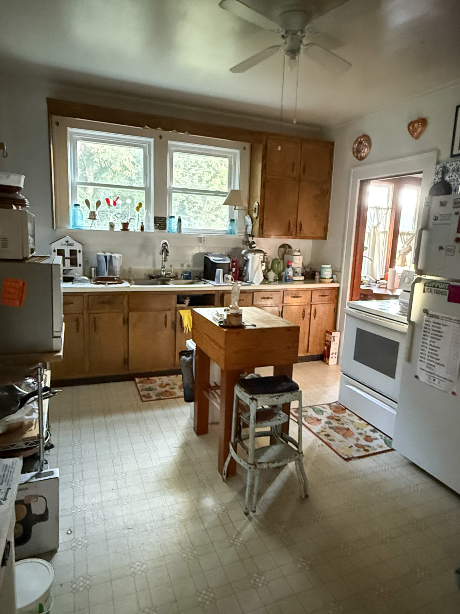 Kitchen with wooden cabinets, white appliances, small island table with stools, and two windows over the sink  inside the home of Sponsored Residential Provider Tammy Hunt in Floyd, Virginia.