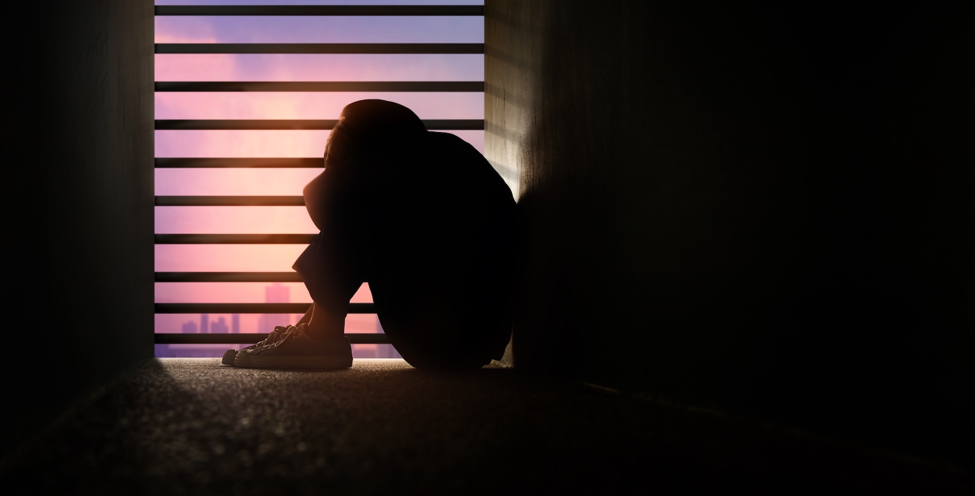 Person curled up in windowsill with head in arms clearly upset