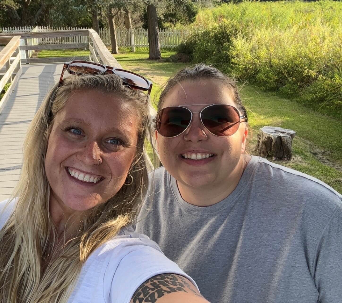 Two women smiling into the camera standing outside on a sunny day